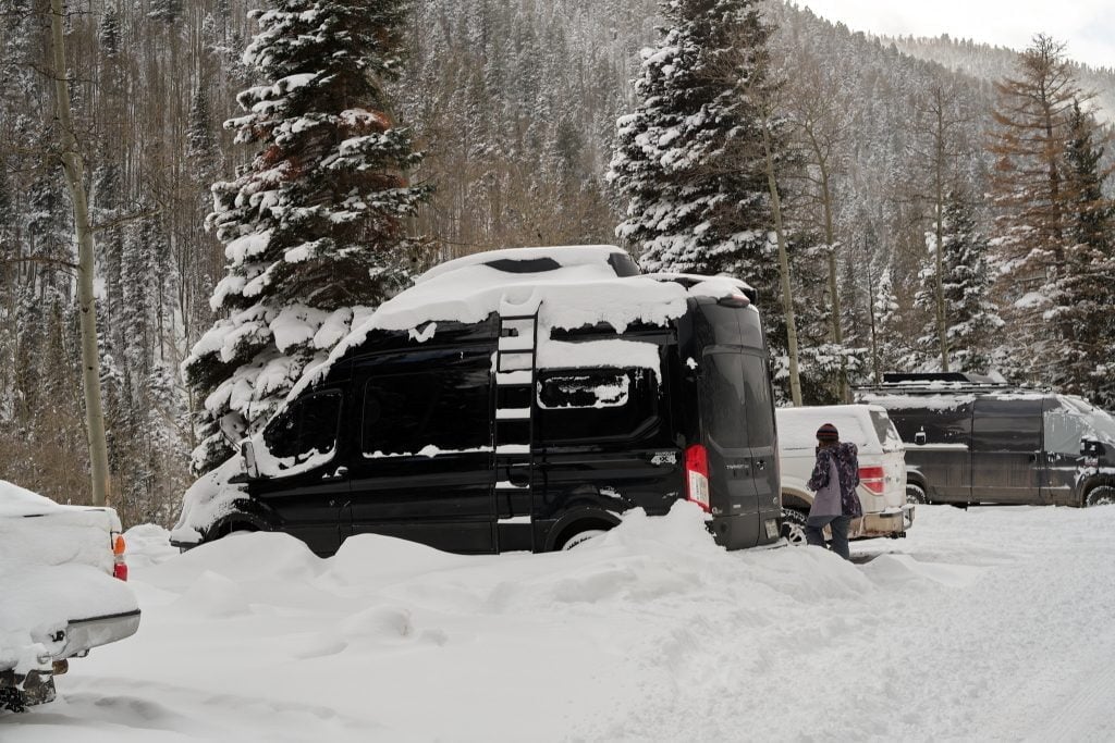 Four-season camper van covered in snow at a mountain campsite