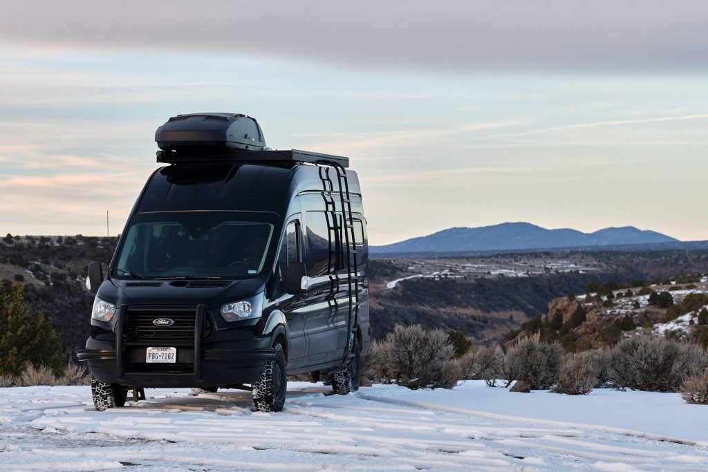 Camper van on fresh snow overlooking a valley at dusk