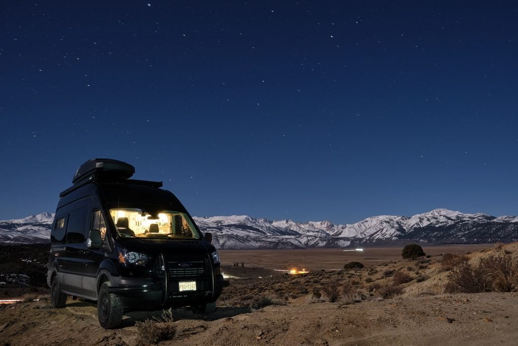 Camper van glowing warm inside on a cold night below snowy mountains
